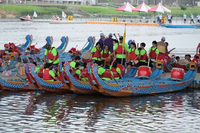 Teams in bright shirts sitting in dragon boats with carved heads by the shore
