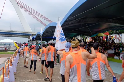 Rowers in orange shirts walking in a crowd under a riverside tent