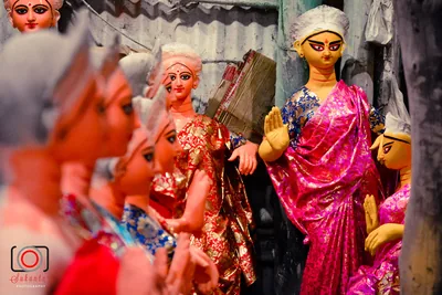 Rows of goddess idols in pink, gold and blue saris waiting to be finished
