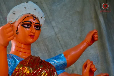 A clay idol of the goddess with a blue sari and orange arms, still being painted
