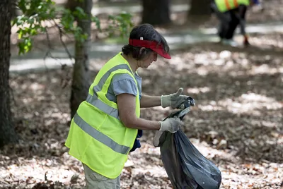 A volunteer in a bright vest picking up litter under trees