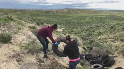 Two people lifting an old tyre out of sandy ground
