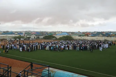 A large crowd gathered for prayer on an open field, seen from a distance