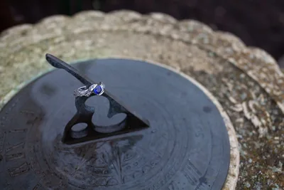An engagement ring resting on a stone sundial in the rain