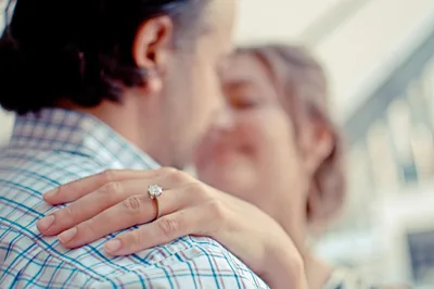 A couple in a warm hug, the woman's hand with an engagement ring on his shoulder