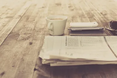 A cup of tea beside a folded newspaper on a wooden table