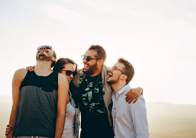 Four friends laughing together outdoors with arms around each other