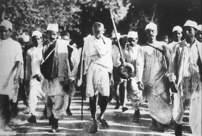 Black and white photo of Gandhi walking with a staff at the head of a line of marchers