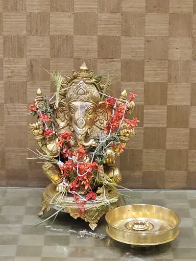 A brass Ganesha idol decorated with red and white flowers beside a puja plate