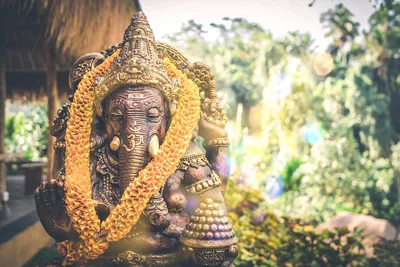 A dark stone Ganesha idol wearing a marigold garland