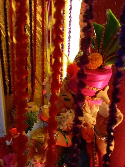 A Ganesha idol seen through hanging strings of red and orange flowers