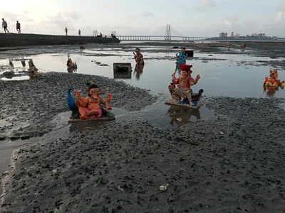 Ganesha idols resting on the wet sand of a beach at low tide, a sea bridge in the distance