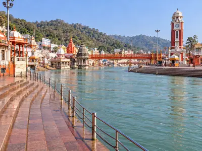 Wide stone steps and railings along the clear blue Ganga, with temples and hills behind
