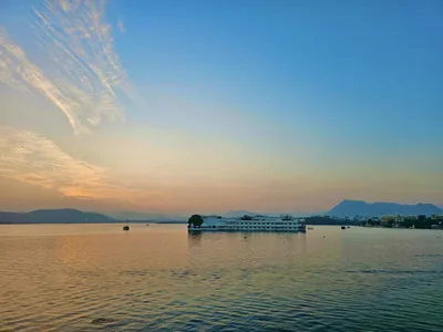 Sunset over a calm lake with hills on the far shore and a white palace on the water