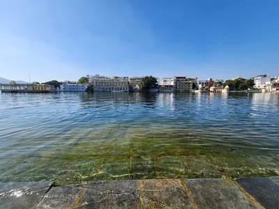 Clear lake water lapping at stone steps with old buildings along the far shore