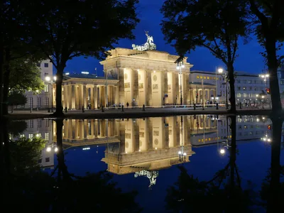 The Brandenburg Gate glowing at night and reflected in still water