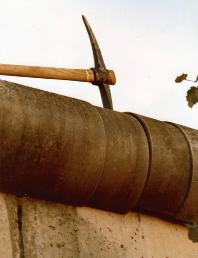 A pickaxe raised against the rounded top of a concrete wall