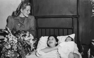 An old photo of a hospital patient smiling with flowers by her bed