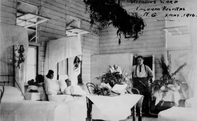 An old photo of a hospital ward with beds and flowers