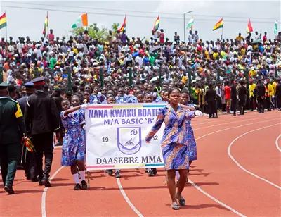 Marchers in matching blue dresses walk behind a school banner on a red track