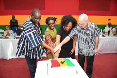 People in kente and smocks cut a cake decorated as the red, gold and green flag