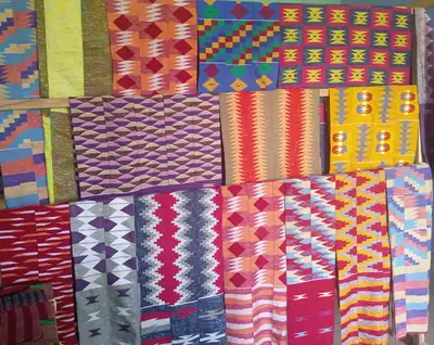 Many bright kente cloths in red, yellow, green and blue patterns laid side by side