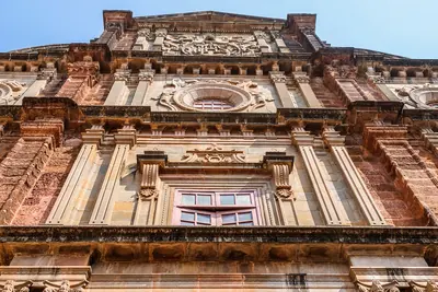 Looking up at the carved stone front of an old church in Goa against a blue sky