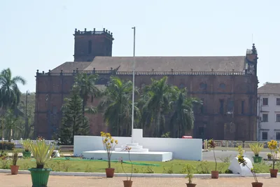 A large old church with a square tower behind a lawn with a white flag post and palm trees