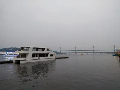 A white cruise boat on a wide river with a long bridge in the distance