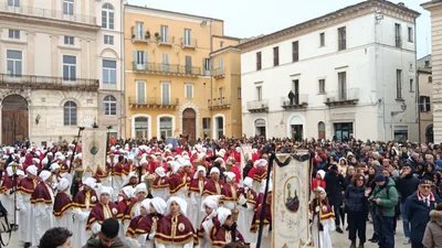 Hooded members of a brotherhood walk in procession in a town square