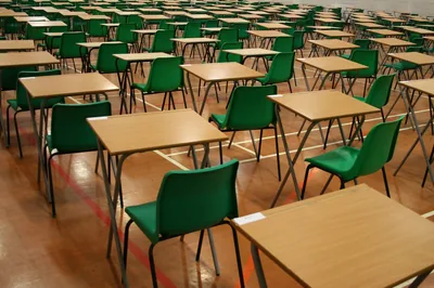 Rows of empty desks and green chairs in an exam hall