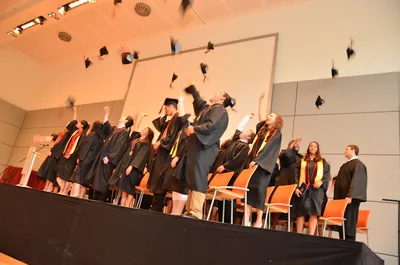 Graduates in black gowns throw their caps in the air in a hall
