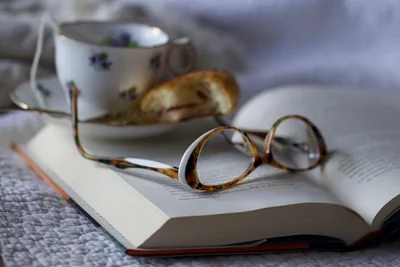 Reading glasses on an open book beside a teacup