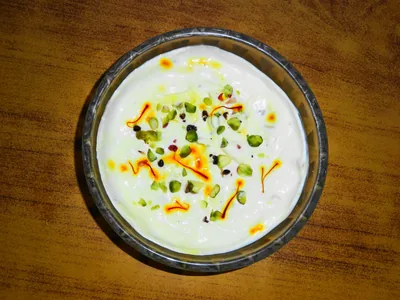 A bowl of creamy shrikhand topped with saffron and chopped pistachios