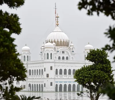 A white gurdwara with domes beside a pool