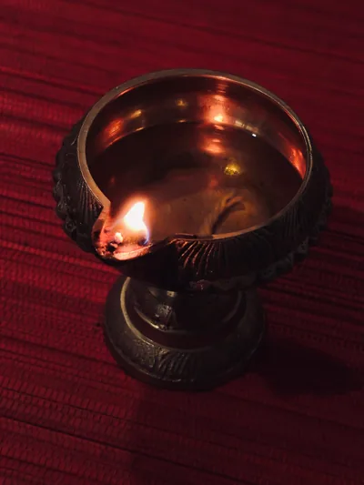 A brass oil lamp burning on a deep red background
