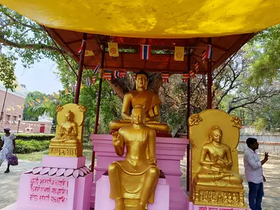 Golden statues of the Buddha seated under a red canopy in a garden