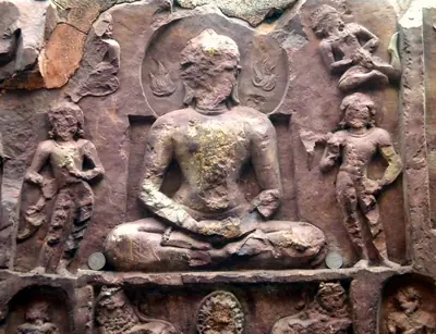 An old stone carving of the Buddha seated in meditation with listeners around him