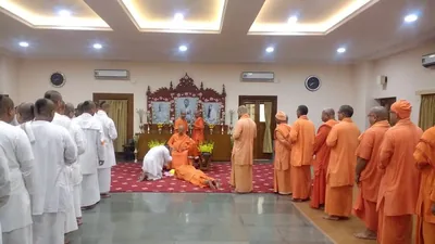 Monks in saffron robes in a prayer hall as a devotee bows before the altar