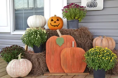 A porch with a carved jack-o-lantern, white pumpkins, flowers and hay bales