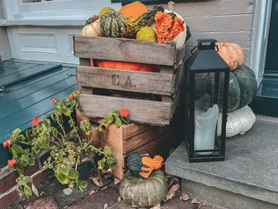A wooden crate of small pumpkins and gourds next to a lantern on the doorstep