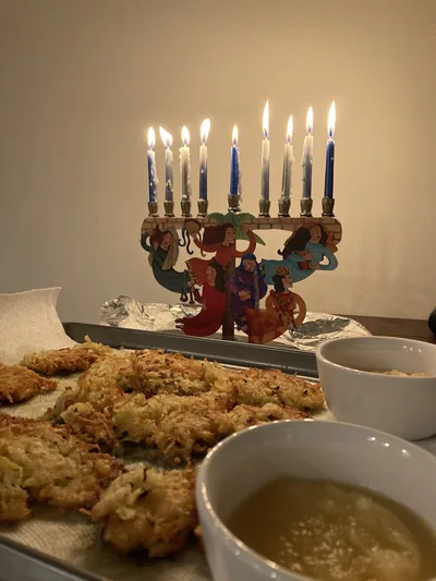 A lit menorah on a table beside a plate of potato latkes