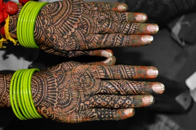 Hands covered in detailed mehndi designs, with green bangles at the wrist