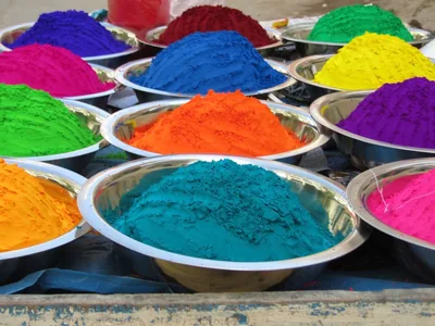 Steel bowls heaped with bright Holi colour powders in blue, orange, pink and green