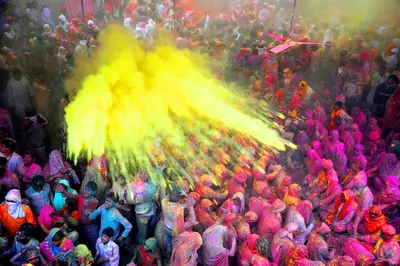 A cloud of yellow colour powder thrown over a huge crowd in a temple courtyard