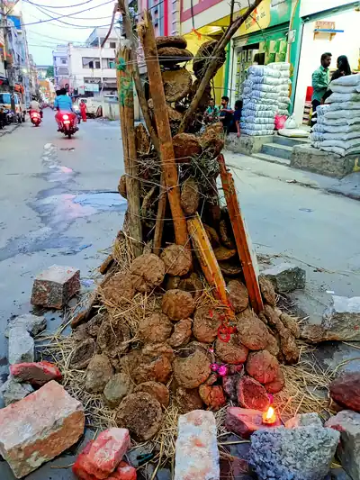 A pile of cow dung cakes and wooden poles set up on a street, with a small lamp