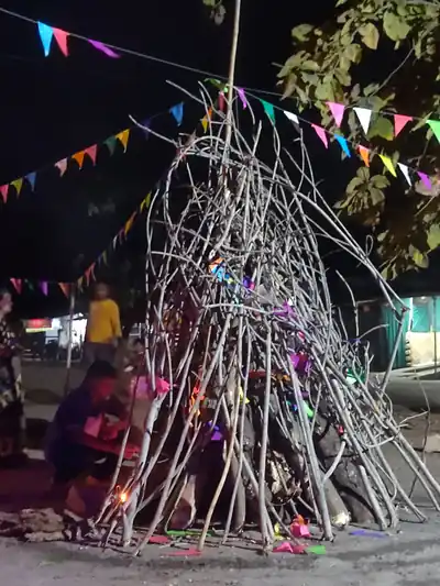 A tall pile of dry branches under strings of colourful flags at night