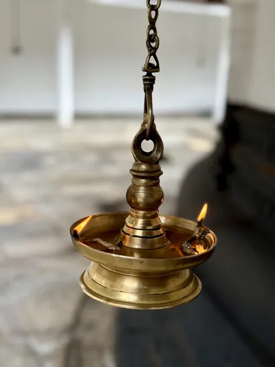 A lit brass hanging lamp with a small flame
