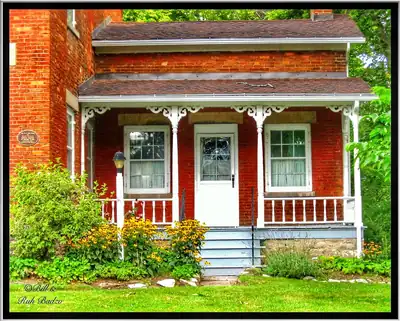 The porch of a red brick house with white railings and flowers