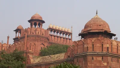 The red sandstone walls and domed towers of the Red Fort against an evening sky